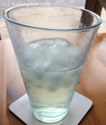 Glass half filled with elderflower cordial and ice cubes.